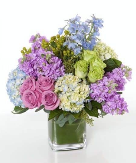 A garden-style cube arrangement in soft pastel colors includes lavender and green roses, hydrangea, stock and more.