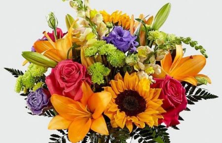 An instant mood booster with it's mix of bright bold colors, this gorgeous fresh flower arrangement brings together sunflowers, hot pink roses, purple double lisianthus, orange LA Hybrid Lilies, yellow snapdragons, green button poms, and lush greens to make this day, their best day. Presented in a clear glass vase, this fresh flower arrangement is made just for you