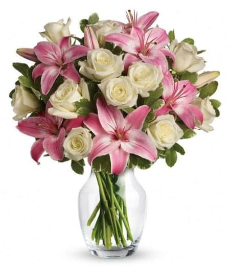 An eye-catching display of roses and lilies is perfectly arranged in a feminine vase which makes a beautiful and lasting impression.