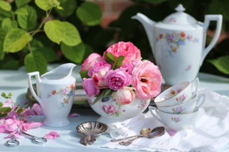 Tea party in garden: vintage china set floral pattern, metal tray, silver ton spoons, tea strainer on linen napkin, garden scissors, rose bowl with roses, outdoor and space, daylight, sunlight